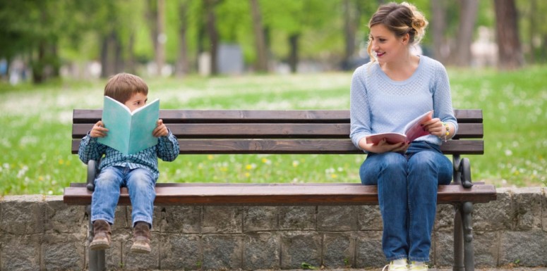 woman and little boy reading at opposite ends of a park bench